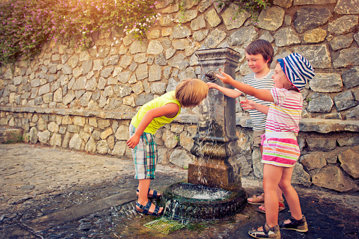 Three happy children having fun with a fountain un summer heat