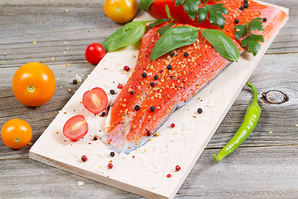 Fresh Salmon and ingredients on Wooden Cooking Plank Closeup horizontal front view of raw red salmon, skin side down, on maple wood grilling plank with seasoning and other herbs sockeye salmon filet stock pictures, royalty-free photos & images