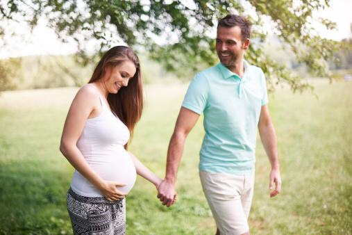 Pregnant woman with husband walking on meadow
