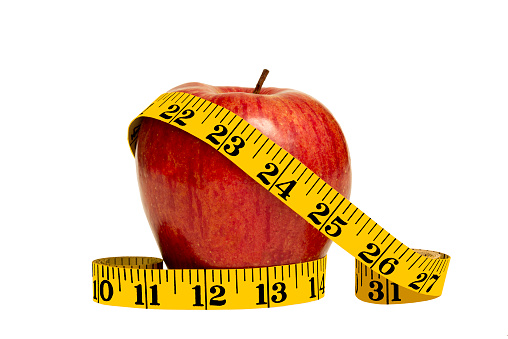 Diet concept. Close up shot of a big shiny red apple and yellow tape measure.  On white background