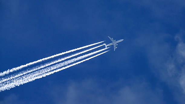 Jet liner with four white vapour stripes against blue sky stock photo