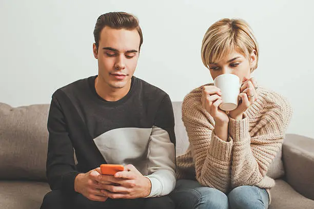 Jealous girl spying her boyfriend's mobile phone while he typing a message