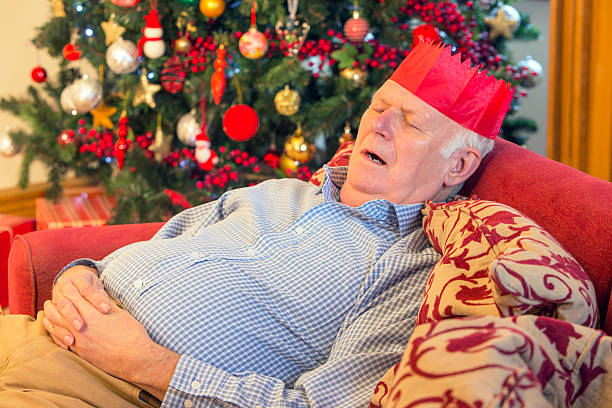 Grandad Sleeping A tired grandfather sleeps on the sofa after Christmas day with a party hat on. sleeping grandpa stock pictures, royalty-free photos & images