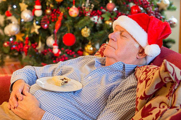 Christmas Snacking A tired grandfather sleeps on the sofa with a mince resting on his belly after Christmas day. sleeping grandpa stock pictures, royalty-free photos & images