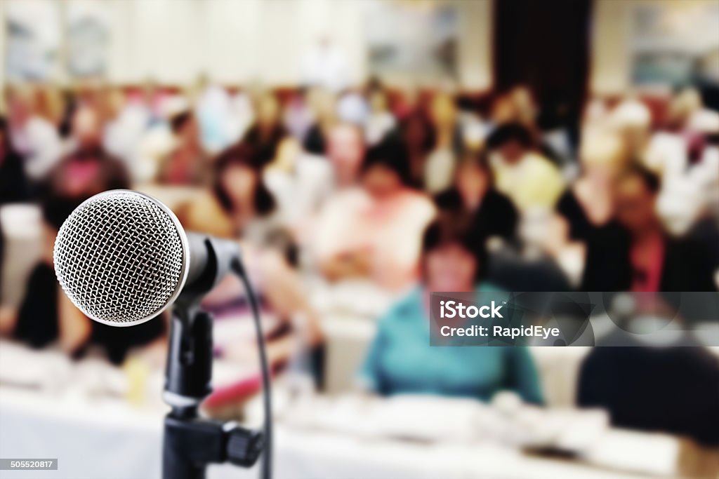 Out-of-focus audience waiting for speaker at seminar An old-fashioned vocal microphone in front of an out-of-focus audience at a meeting, seminar or social occasion. Meeting Stock Photo