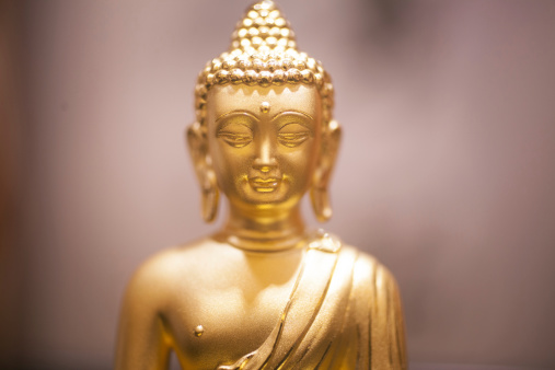 Closeup portrait photo of a Chinese traditional 18 carat solid gold money Buddha wealth statue deity wearing Buddhist clothing and headgear that brings good luck, fortune and financial prosperity.
