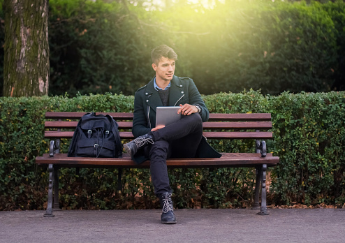 Elegant student sitting on a bench in the park using tablet