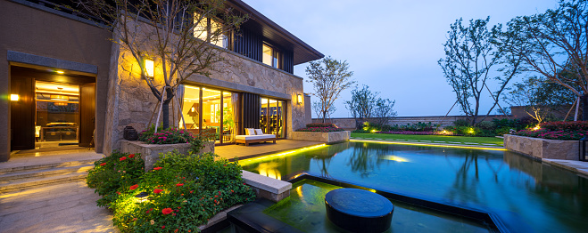 Exterior view of illuminated modern luxury house with swimming pool in foreground at dusk. Luxury lifestyle concept