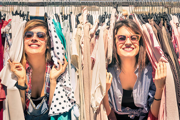 Young beautiful women shopping at the weekly cloth market Young beautiful women at the weekly cloth market - Best friends sharing free time having fun and shopping in the old town in a sunny day - Girlfriends enjoying everyday life moments garment photos stock pictures, royalty-free photos & images