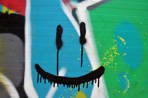 Abstract smiling face on wall with colorful graffiti and splashed paint.