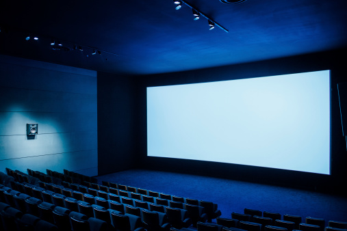 Cinema auditorium with white screen and luxury seats - dark movie theatre ready for projection