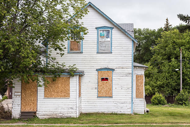 old condemned white two-story house with windows boarded up an old white condemned two-story house with windows boarded up and a sign saying "no trespassing" with a big green tree in front. boarded up photos stock pictures, royalty-free photos & images