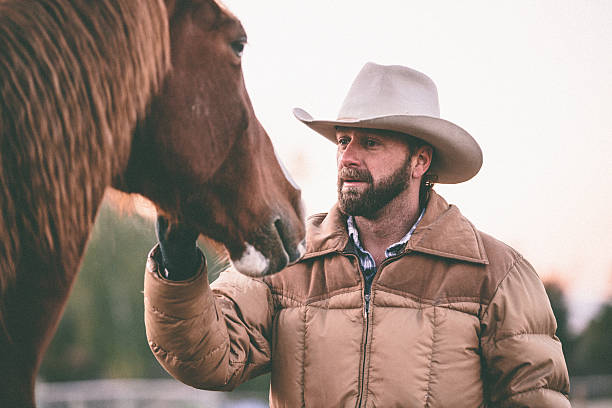 istock Working man with cowboy hat stands petting horse 505561535