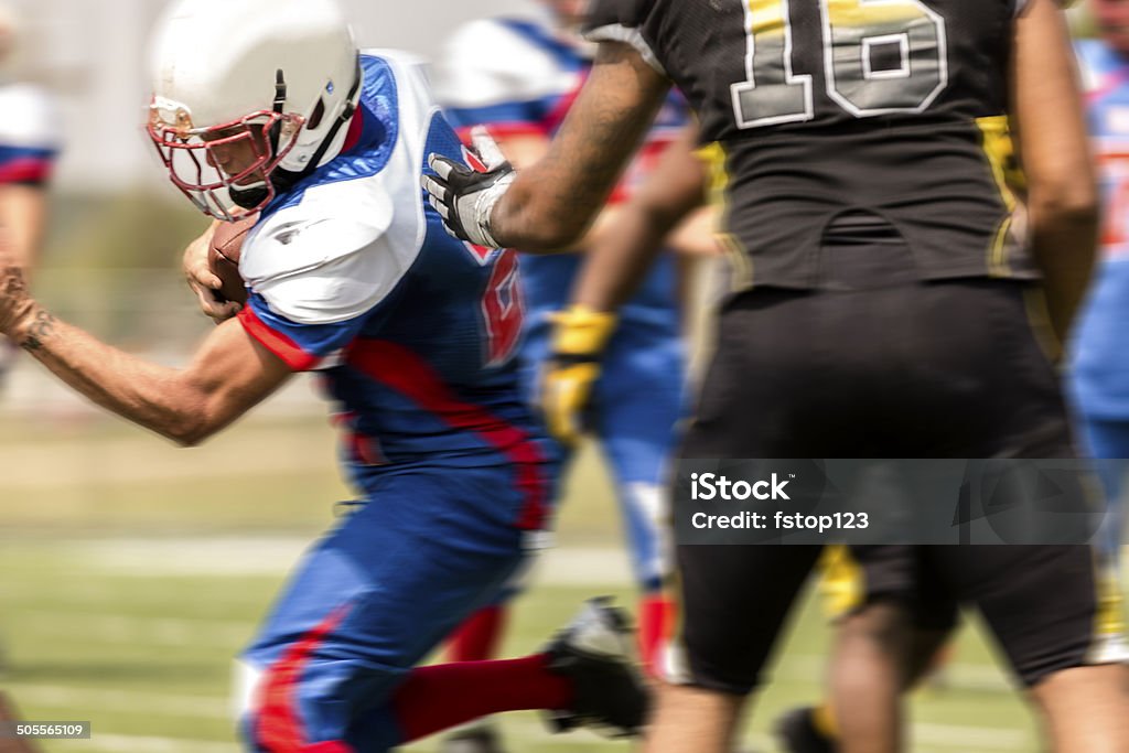 Football running back carries the ball. Defenders. Football team's running back carries the football. Defenders around him. Blurred motion. Adult Stock Photo