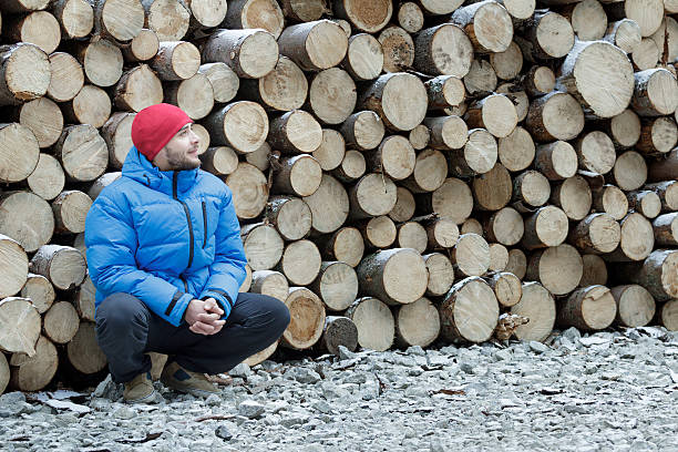 Hunkering worker at pile of logged firewood background
