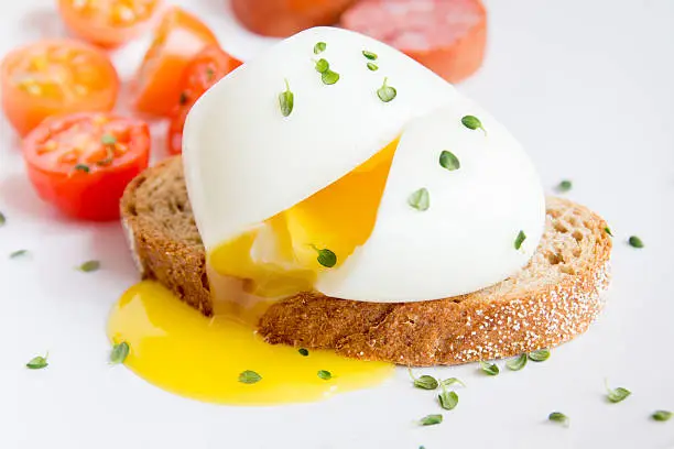 Poached egg on piece of wholegrain bread with vegetables and herbs close up