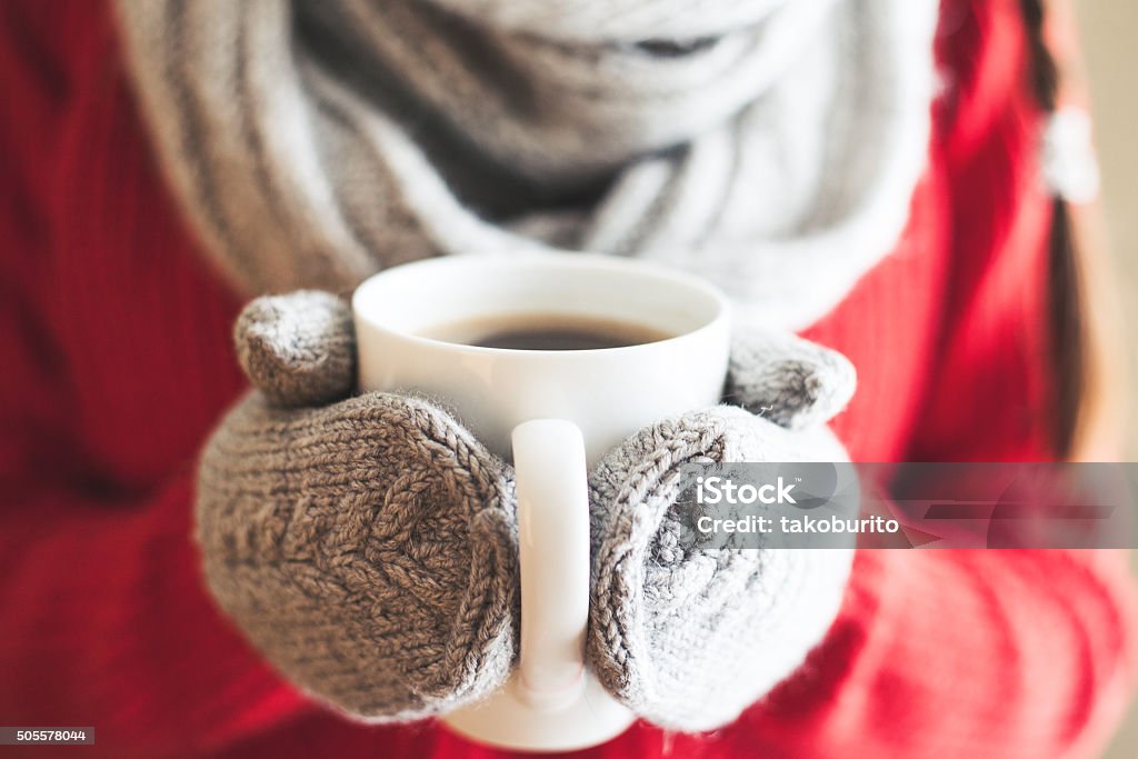 Woman hands in gloves holding a mug Female hands holding hot mug close up. Woman hands in woolen mittens holding a cup with hot cocoa, tea or coffee. Cold Temperature Stock Photo