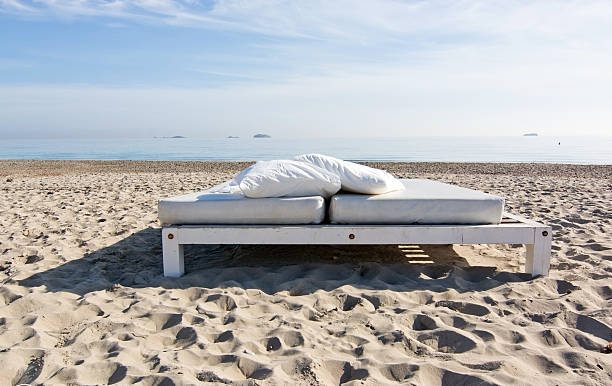 White sunbed on sandy beach with ocean view on a sunny morning in Ibiza, Spain.