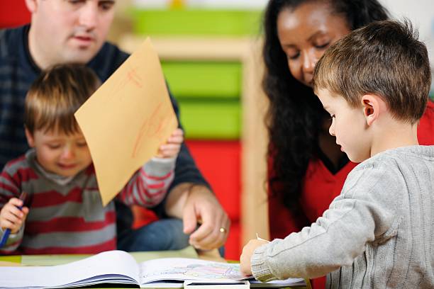 istock Little Boy Drawing/ Writing While Carers Supervise Younger Children 505583013