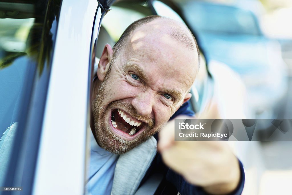 Enraged driver, face a mask of fury, loses his temper A furiously angry man driving yells, hanging out of the window and pointing at someone accusingly in a bout of road rage! Adult Stock Photo