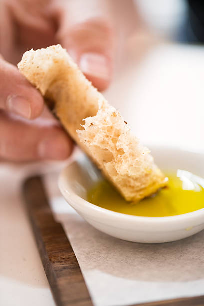A man dips a torn piece of hand made artisan bread in extra virgin olive oil.
