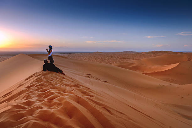 пара наслаждаясь закат erg chebbi песчаные дюны, марокко, северная африка - landscape desert wave pattern erg chebbi dunes стоковые фото и изображения