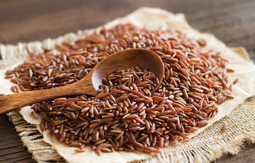 Uncooked Red rice with a wooden spoon close up