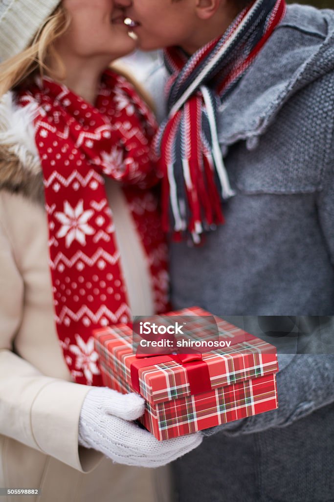 Christmas surprise Image of amorous guy giving his girlfriend Christmas present while kissing her Adult Stock Photo