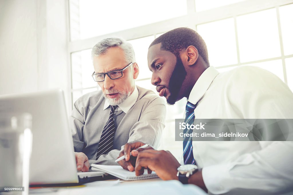 Concept for teamwork and knowledge transfer Photo of aged businessman and his colleague. Businessmen working in office with big window. Men using laptop Senior Adult Stock Photo