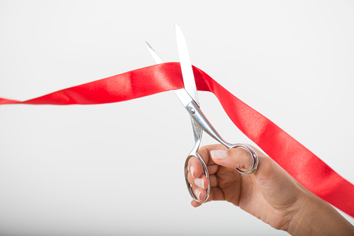 Hand cutting red ribbon with scissors.