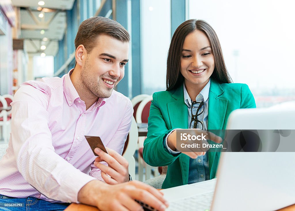 Young couple buying new items on internet auctions and smiling Portrait of hansome young man and attractive young woman, heterosexual couple sitting in front of laptop and ordering items on e-shop. Man is holding golden credit card while woman is pointing on the items on screen. Image taken with Nikon D800 and 24-70 lens, developed from RAW in XXXL size. Location: Novi Sad, Serbia, Europe 20-24 Years Stock Photo