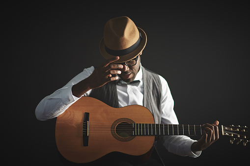 Elegant young man in smart clothes and hat holding guitar