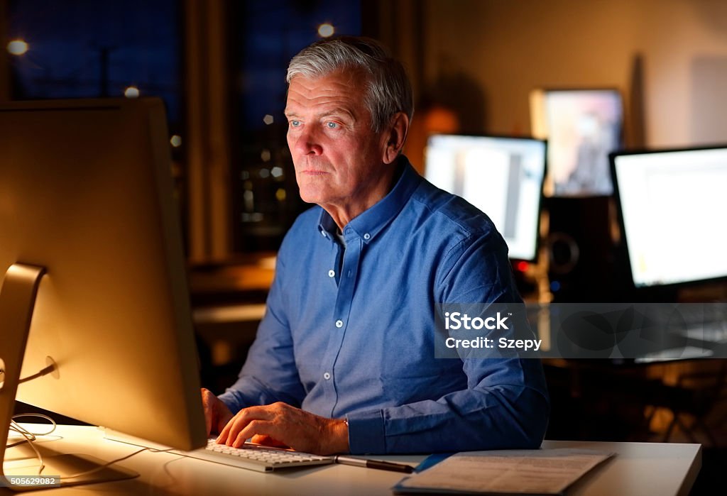 Working late Portrait of senior creative director sitting at agency and and working hard in front of computer at late. Active Seniors Stock Photo