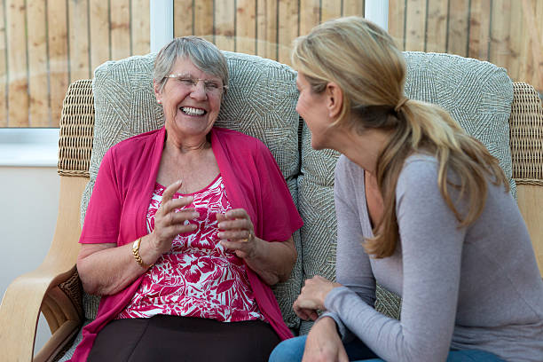 Daughter Visiting Her Senior Mother An adult daughter is sat with her senior mother. They are chatting to one another and smiling. father daughter 80s stock pictures, royalty-free photos & images