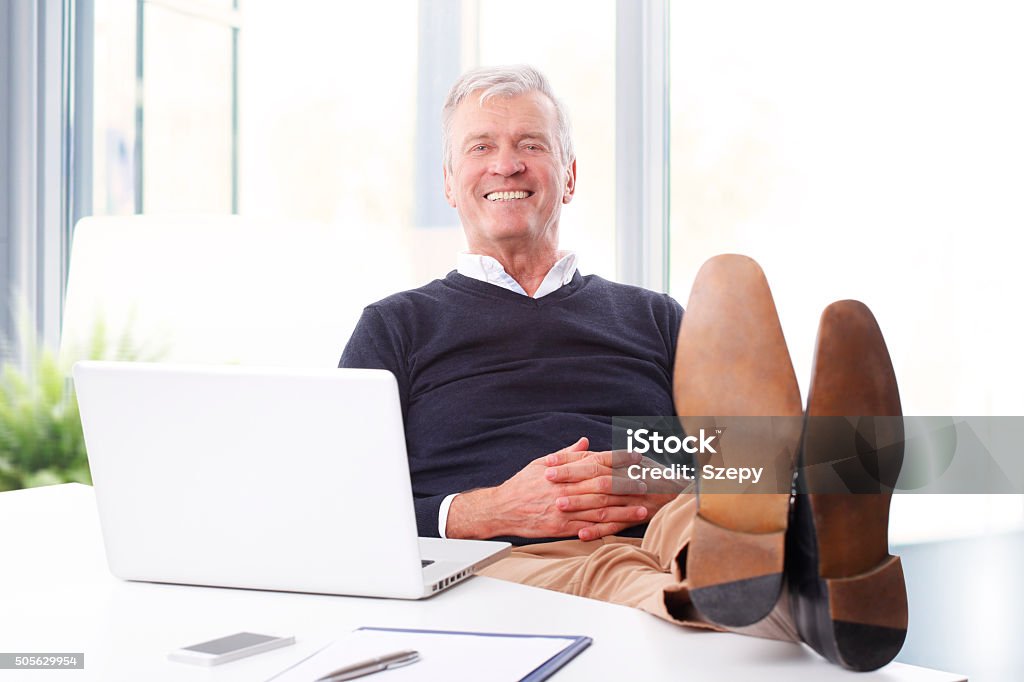Senior businessman portrait Portrait of satisfied senior businessman sitting at workplace in front of computer and looking at camera while relaxing. Old professional man feet on office desk. Financial Advisor Stock Photo