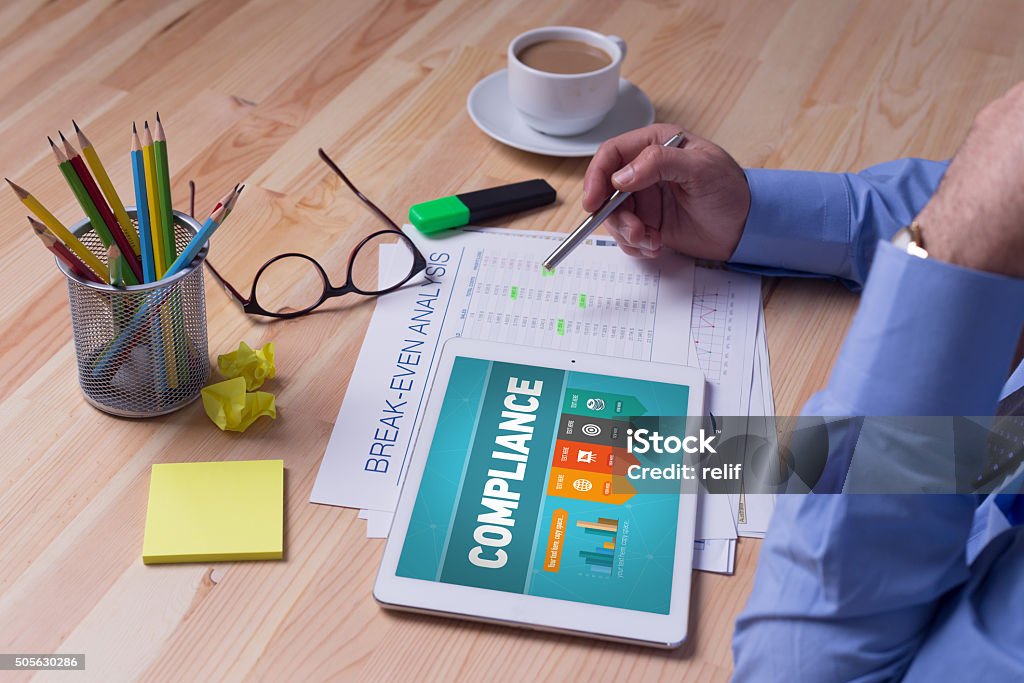 Man working on tablet with COMPLIANCE on a screen Conformity Stock Photo