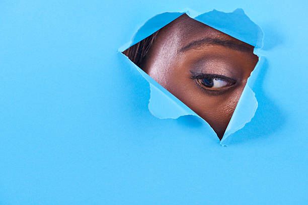 What's that down there? A view of a woman's eye looking through a hole in some colorful paper emergence photos stock pictures, royalty-free photos & images