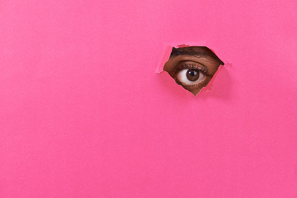I see you! A view of a man's eye looking through a hole in some colorful paper emergence photos stock pictures, royalty-free photos & images