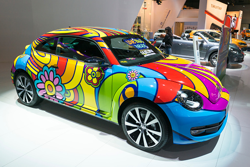 Brussels, Belgium - Januari 12, 2016: Volkswagen New Beetle Love Bug Parade art car retro styled compact car. The car is on display during the 2016 Brussels Motor Show. The car is displayed on a motor show stand, with lights reflecting off of the body. There are people looking around and other cars on display in the background.