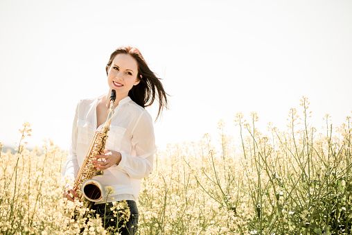 Portrait of young  woman with her saxophone in blossoming rapeseed field