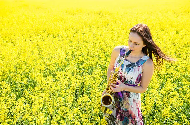 Photo of Woman playing saxophone in rapeseed field