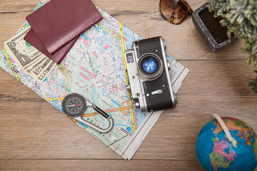 Composition of map, compass, camera, globe, passport, money, sunglasses and plant on wooden desktop