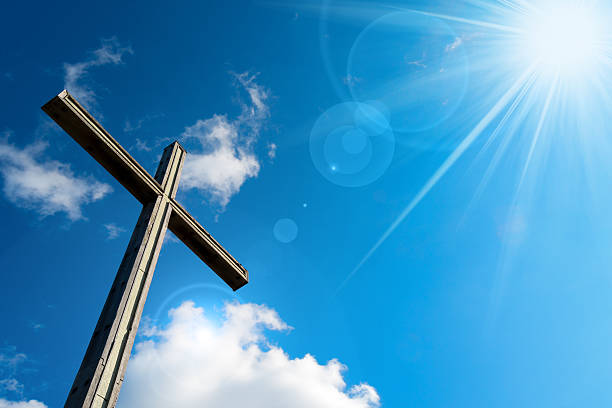 Wooden christian cross on blue sky with clouds and sun rays