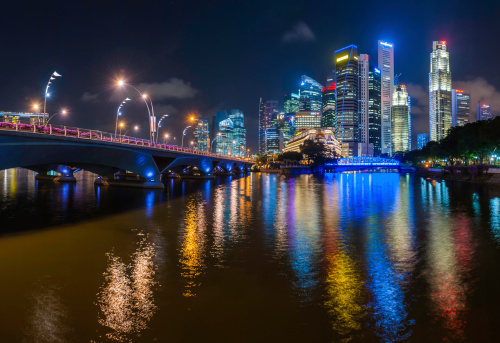 The neon lights and colourful glow of illuminated skyscrapers and luxury hotels in the heart of Singapore's crowded Central Business District reflecting in the tranquil waters of the Singapore River below the Cavenagh Bridge. ProPhoto RGB profile for maximum color fidelity and gamut.
