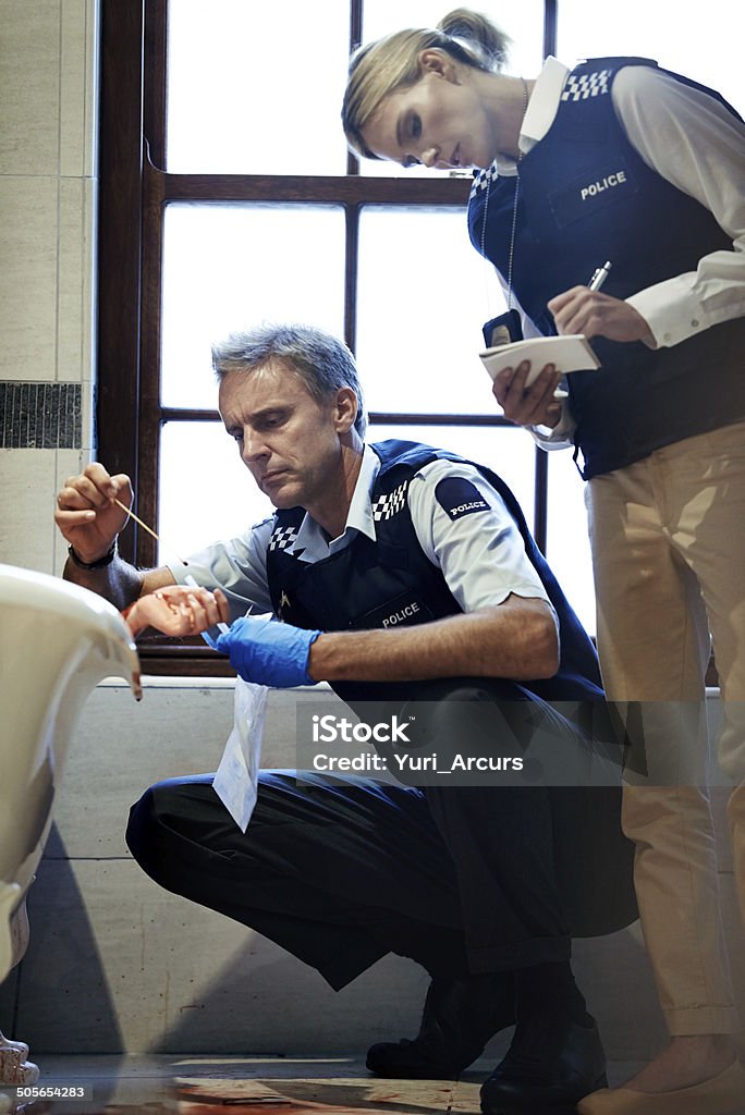 Taking samples from the deceased Shot of two investigators working their way through a bloody crime scene Forensic Science Stock Photo