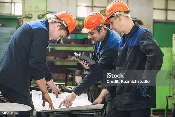 Men With Drawings Working In An Old Factory To Install Stock Photo - Download Image Now