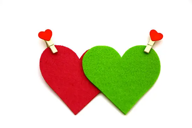 Red and green colored heart shapes made of felt with decorative pins, shot on white.