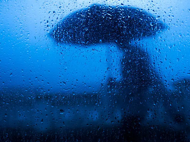 Blurry silhouette through car glass rainy of men with umbrella.