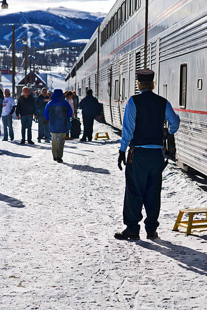 Amtrak "California Zephyr" Frasier, Colorado, USA - January 5, 2016: An Amtrak conductor from the "California Zephyr" train surveys the scene as passengers disembark with the Winter Park Ski Resort seen in the distance. Amtrak stock pictures, royalty-free photos & images