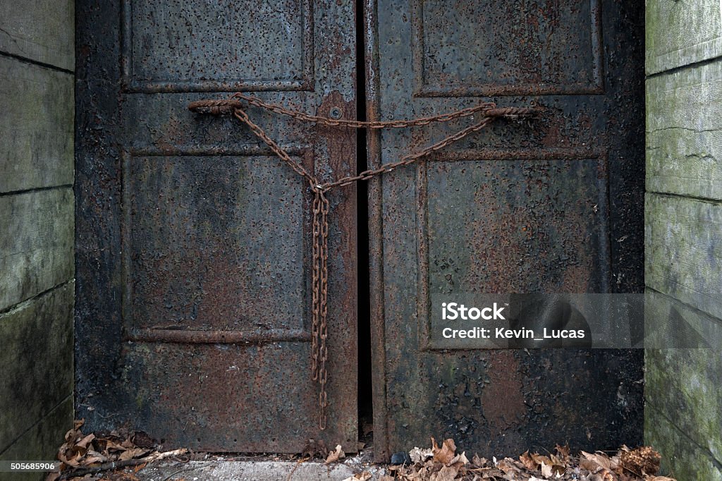 Rusty Door with Chain A very old rusty iron door is heavily chained shut.  Dry leaves rest in fron tof it.  Closely cropped. Cemetery Stock Photo
